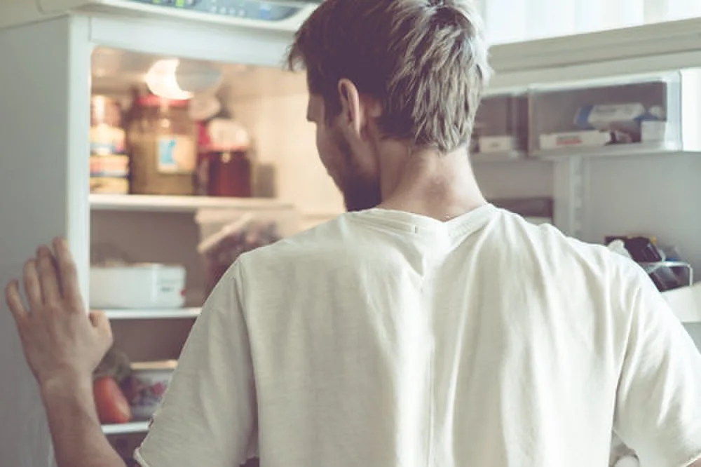 Bearded man standing near the opened fridge at home kitchen.